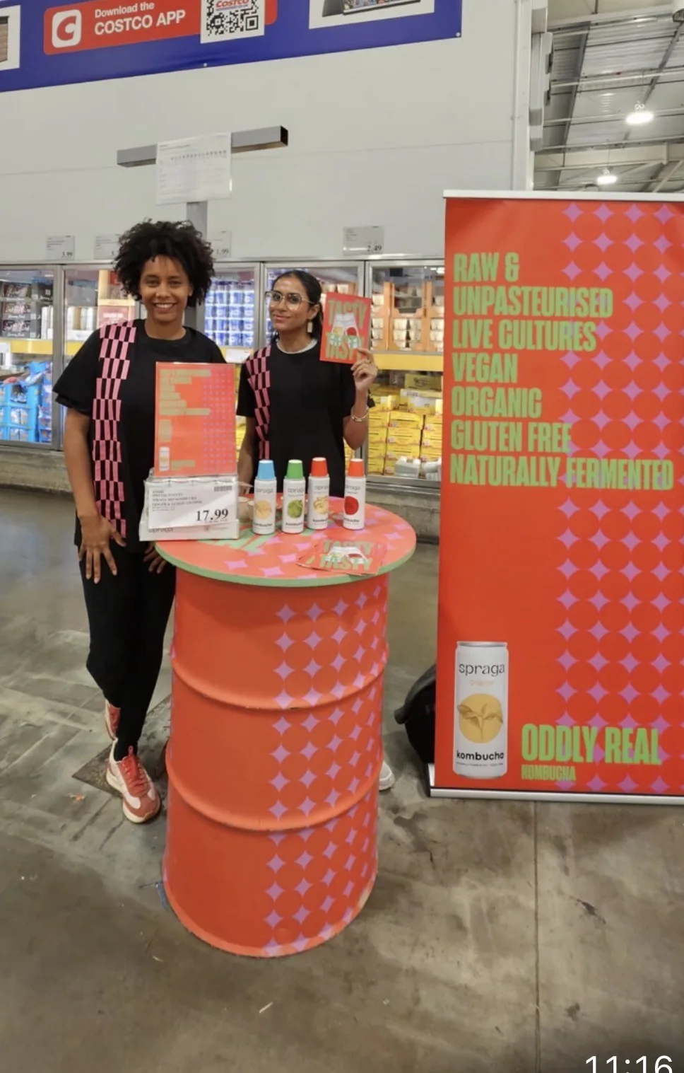 Retailer Engagement: FOTS ambassadors at the Spraga kombucha tasting barrel with cans, booklets and the Oddly Real roll-up banner inside Costco