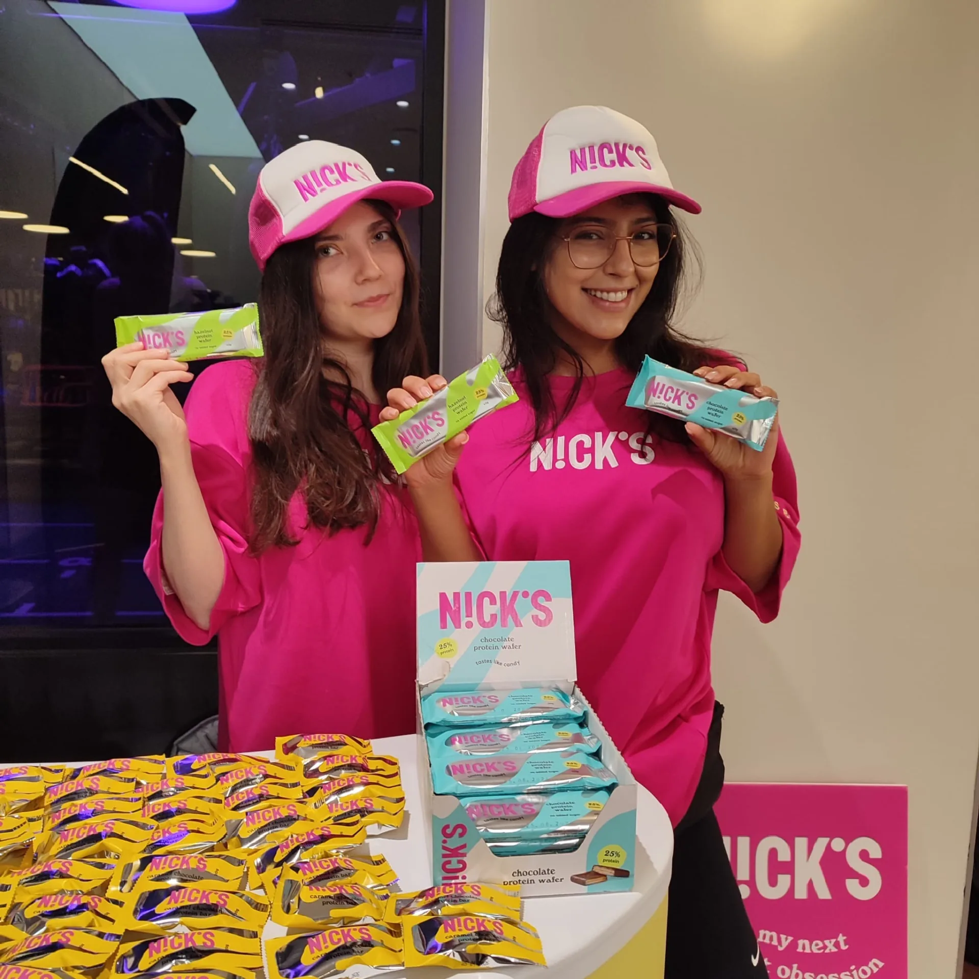 Two FOTS brand ambassadors in Nick's pink T-shirts and caps behind a table of Nick's protein bars and wafers