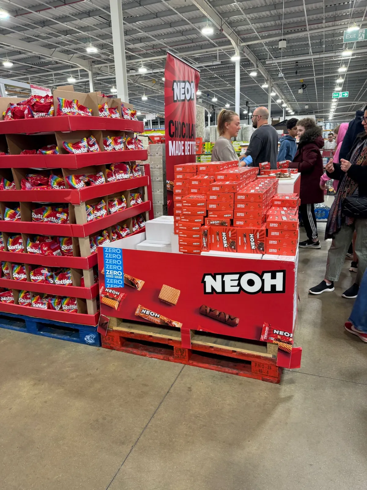 NEOH pallet display stacked with Zero Added Sugar packs alongside a busy tasting stand in a wholesale club