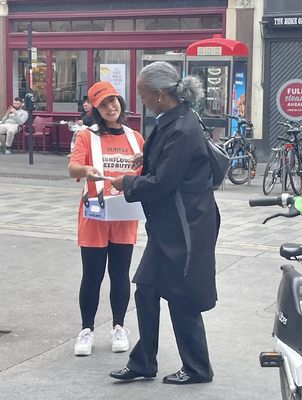 FOTS ambassador in Sunfly kit handing a Sunflower Seed Butter sample to a shopper on a London high street