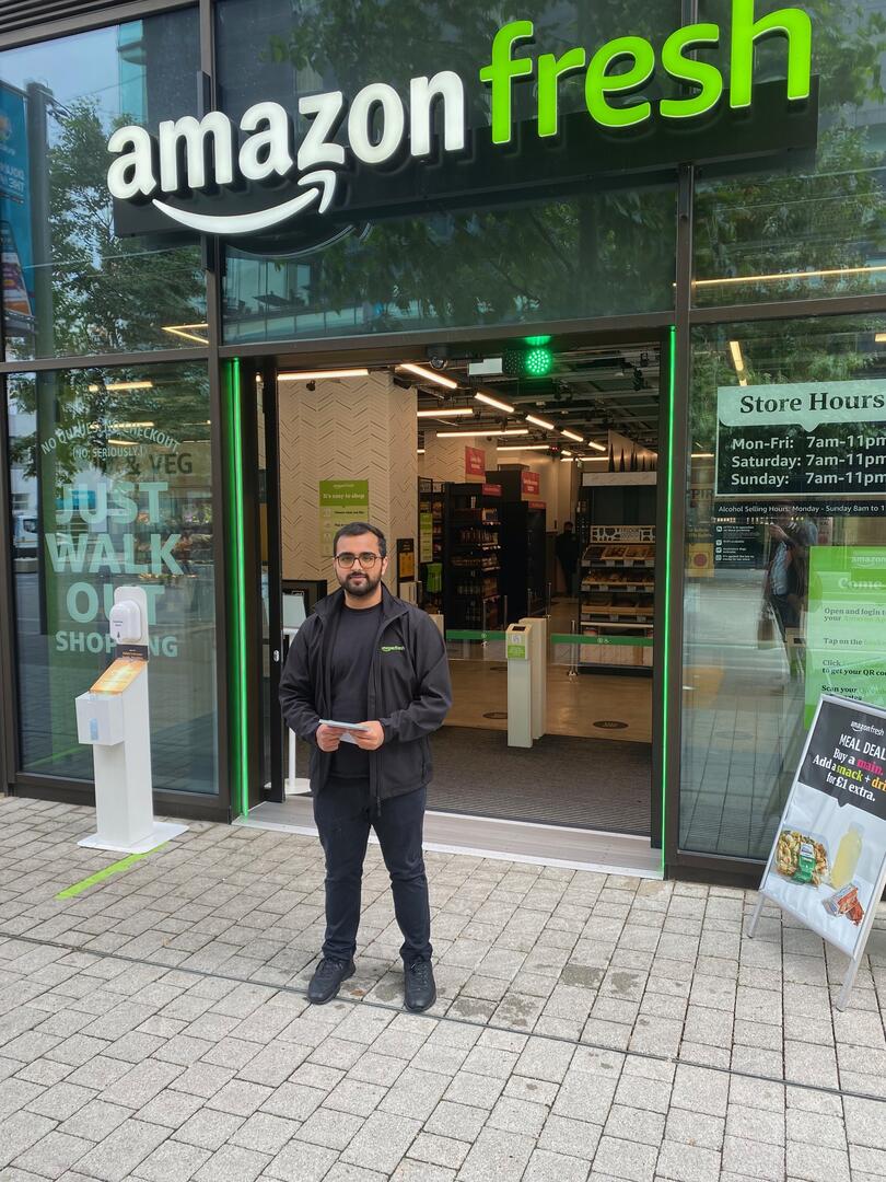 man standing outside amazon fresh store holding leaflet